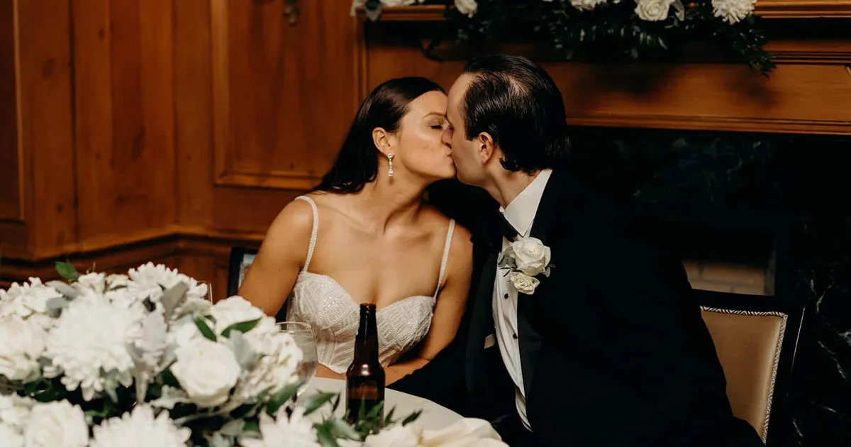 Bride and groom kissing at a table, Summer and Nicholas