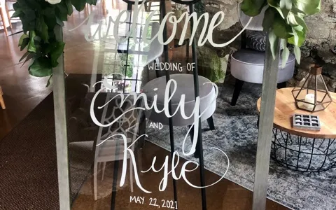 A sign decorate with white flowers that says "Welcome Emily and Kyle"