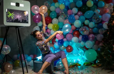 woman using a photo booth with many multi-colored balloons
